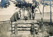 F.M.Smith standing at well on Cedar Island